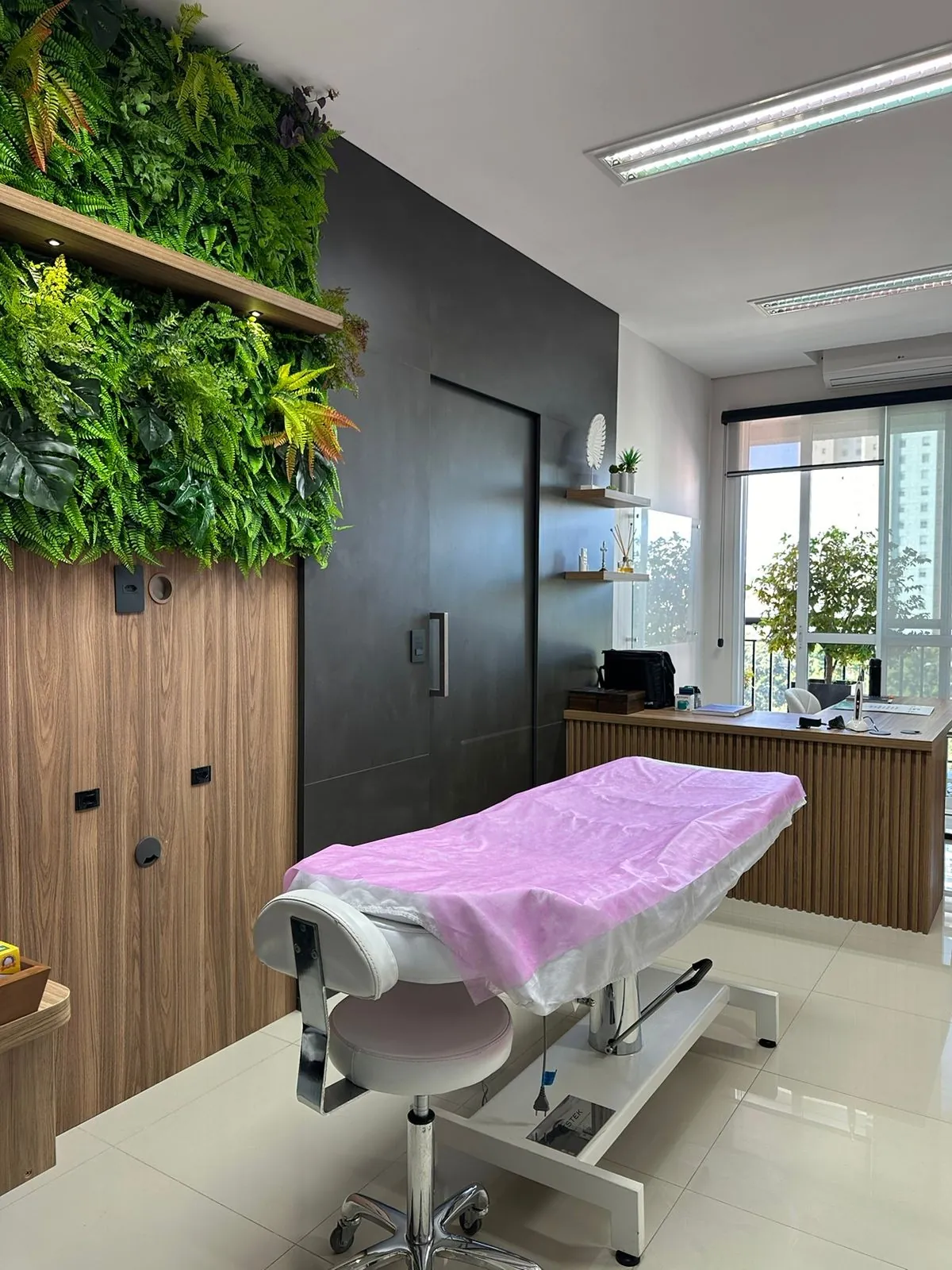 Sala de atendimento do consultório da Dra. Cristiane Felca, com maca, parede verde e janela ampla